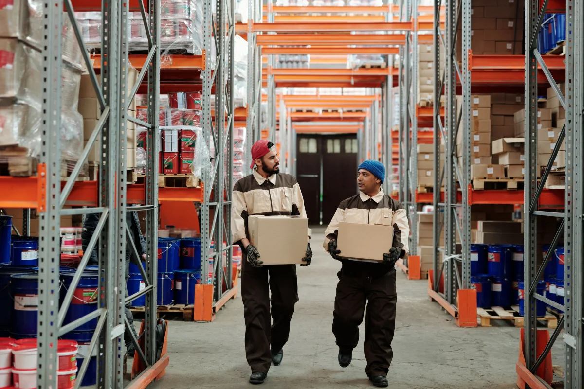 Warehouse workers moving cartons through a storage aisle